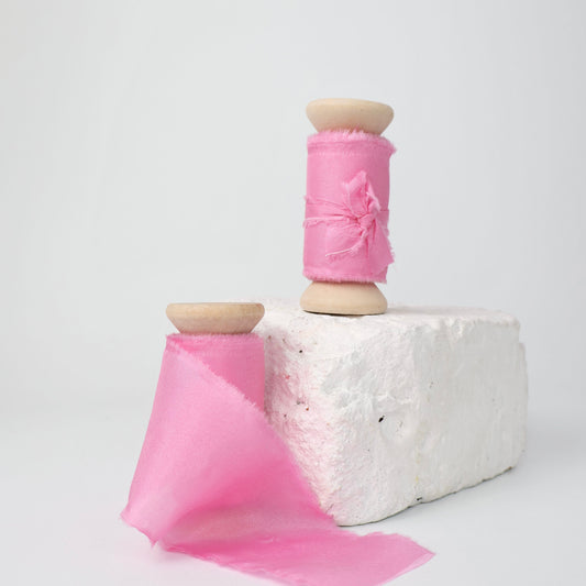 Two spools of bright pink 100% Habotai silk ribbon.